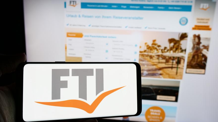 Das Foto zeigt im Vordergrund das Logo der FTI Touristik auf einen Smartphone, im Hintergrund ist die Homepage der FTI Touristik zu sehen