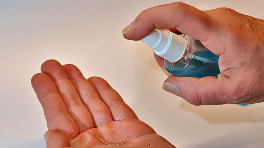 Eine Hand sprüht eine zweite mit Desinfektionsspray ein
